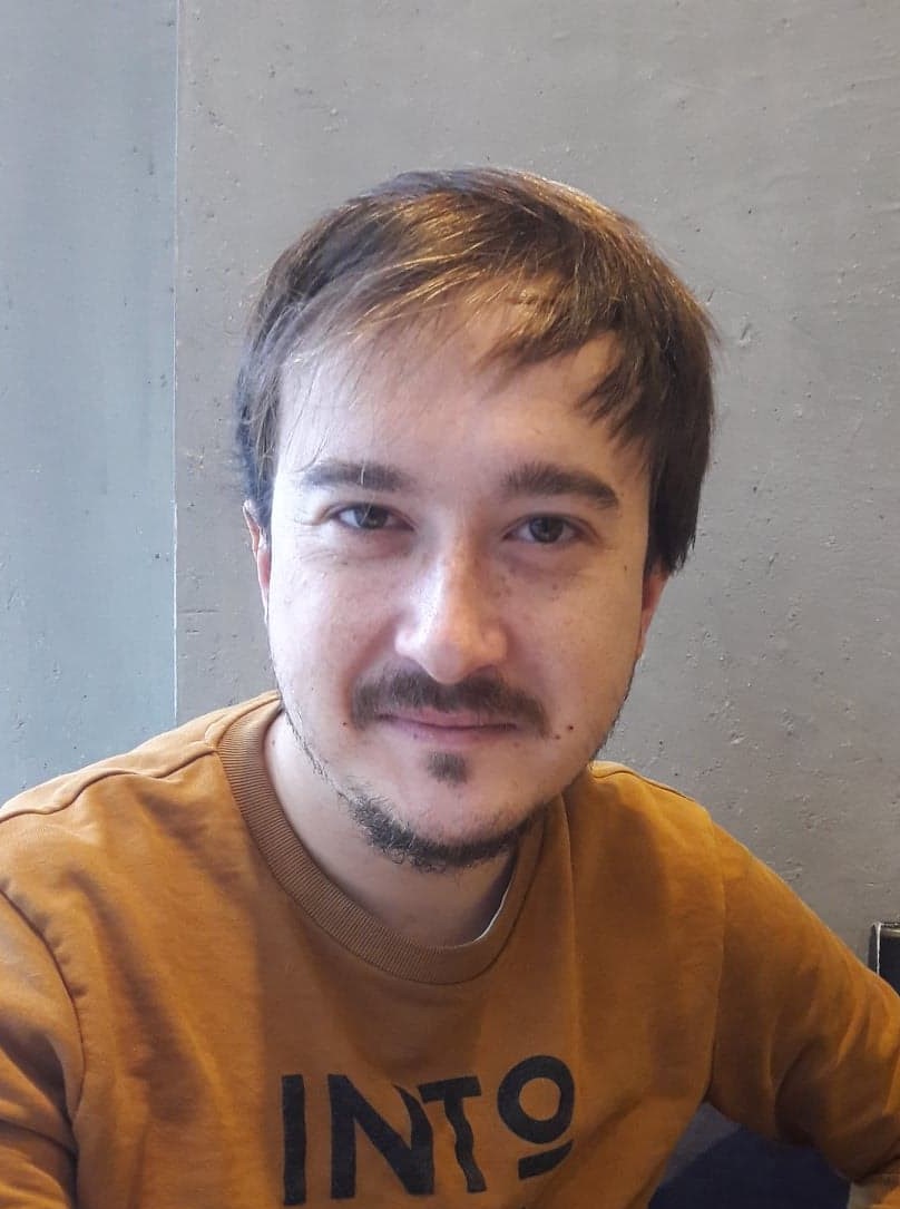 Jeune homme souriant pris en buste avec un pull orange - Valentin Oa écrivain public